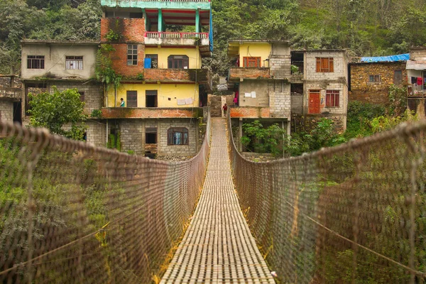 Lano zavěšené visutý most v Nepálu s barevnými vesnice v — Stock fotografie