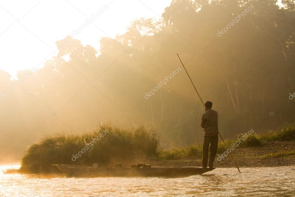 Reflection: man rowing on the boat in the foggy forest on the Narayani River in nepal, chitwan national park rain forest