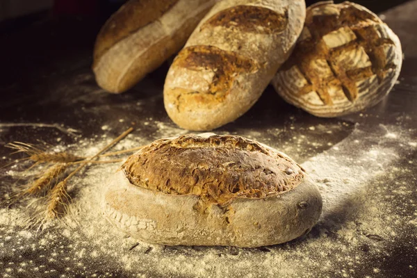 Сельский хлеб и пшеница на черном столе с мукой на нем — стоковое фото