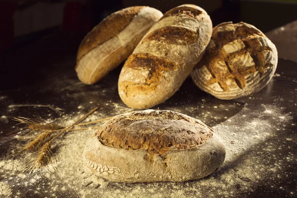 Bauernbrot und Weizen auf schwarzem Tisch mit Mehl darauf — Stockfoto