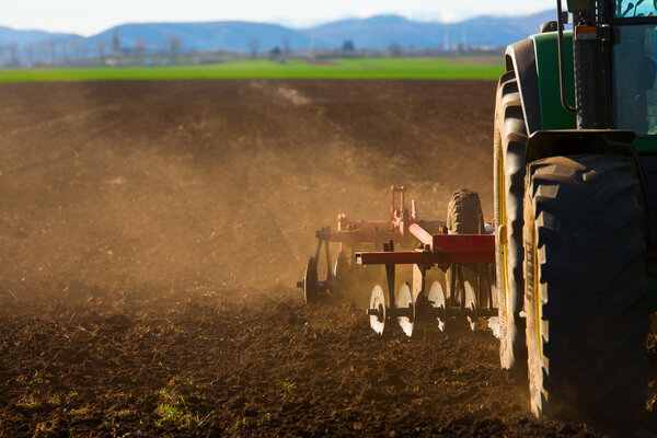 Трактор на закате вспахивает поле
