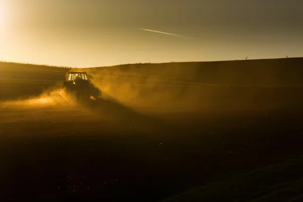 Трактор під час заходу сонця, що оранює поле — стокове фото