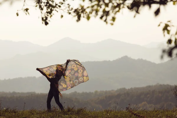 Beautiful young woman jumping on a green meadow with a colored tissue — Stock Photo, Image