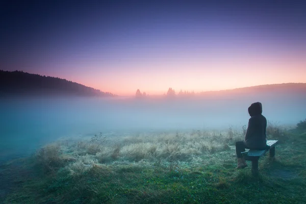 Žena uvolňující na lavičce v mlhavé ráno — Stock fotografie