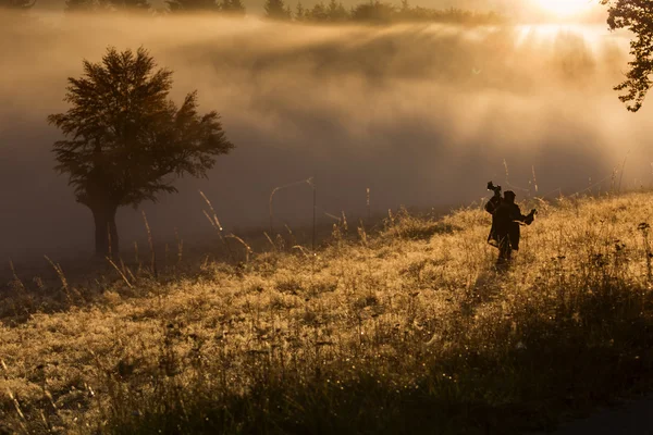 Silhouet van een jonge fotograaf tijdens een mistige sunrise. — Stockfoto