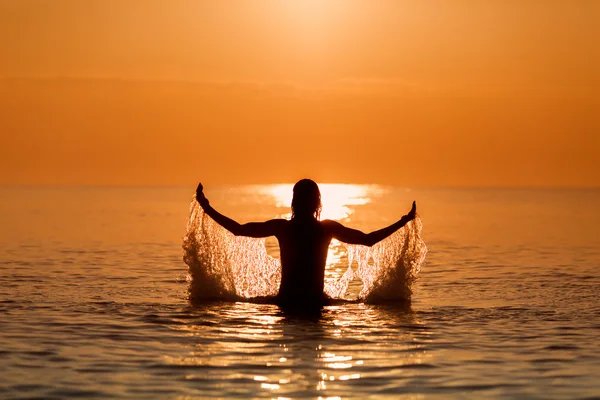 Uomo che spruzza acqua con le mani su un mare all'alba — Foto Stock