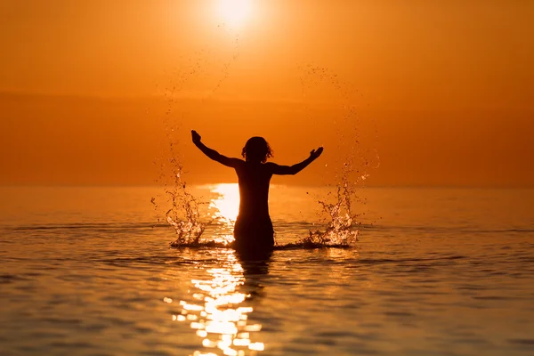 Un bărbat stropind apă cu mâinile pe o mare în răsăritul soarelui — Fotografie, imagine de stoc