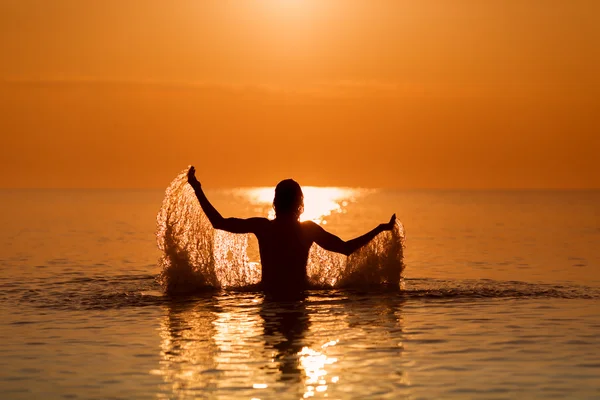 Uomo che spruzza acqua con le mani su un mare all'alba — Foto Stock