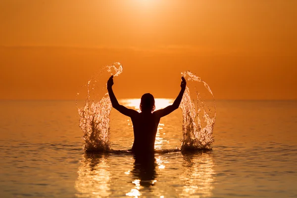 Man Splashing Water dengan tangannya di atas laut saat matahari terbit — Stok Foto