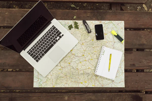 Planning travel on wood table outside with map, laptop, knife, n