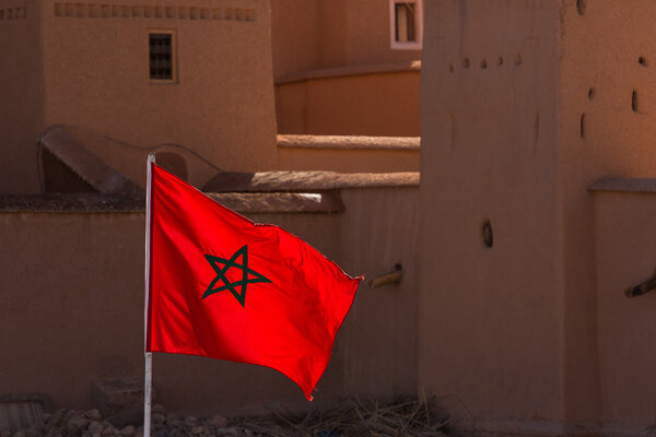 Waving Fabric Flag of Morocco with traditional building in backg