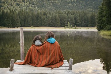 Anne ve kızı bir iskelesi göl ve orman FA ile oturan