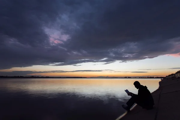 Silueta unui om care citește lângă lac la apusul soarelui — Fotografie, imagine de stoc