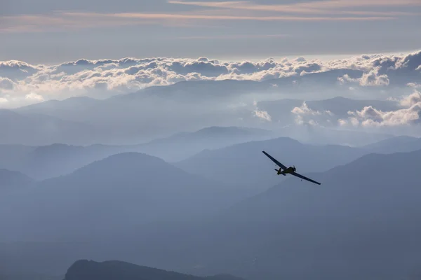 Sillhouette van vliegtuigje over wolken en bergen — Stockfoto