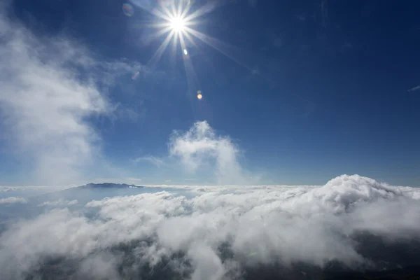 Sol como estrela sobre nuvens fofas sobre as montanhas e o céu azul — Fotografia de Stock