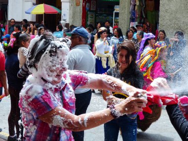 Cuenca, Ekvador - 6 Şubat 2016: Karnaval sırasında düzenlenen geleneksel geçit töreninde kadınlar ve kalabalık birbirlerine köpük püskürtüyor. Herkes eğleniyor..