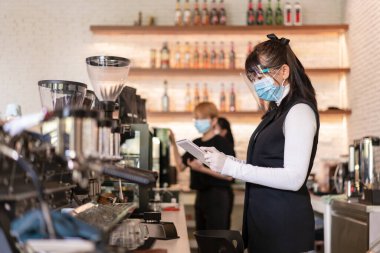 Kahve dükkanında cerrahi maske ve yüz koruyucu takan Asyalı kadın işçi.