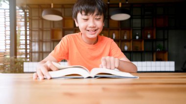 Tahta masada elinde kitapla gülümseyen bir çocuk. Öğrenim, evde eğitim
