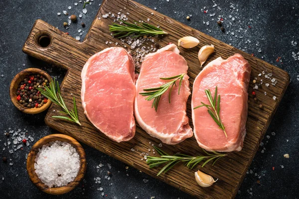 Steaks de porc frais sur planche à découper avec ingrédients pour la cuisson. — Photo