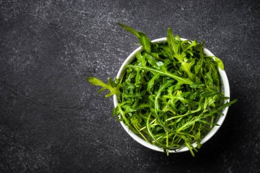 Arugula taze yeşil yapraklar siyah taş masada.