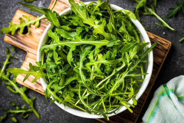 Arugula fresh green leaves at black stone table.
