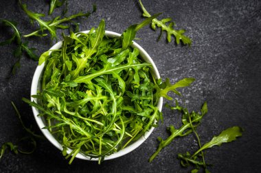 Arugula taze yeşil yapraklar siyah taş masada.