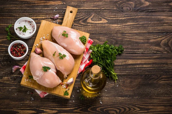 Chicken fillet with ingredients for cooking on wooden table.