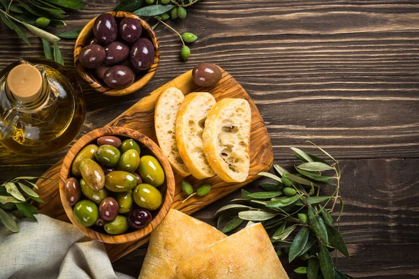 Olives, olive oil and ciabatta on wooden table. — Stock Photo, Image