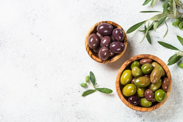 Přírodní řecké olivy v dřevěných miskách a láhev olivového oleje na bílém pozadí. — Stock fotografie