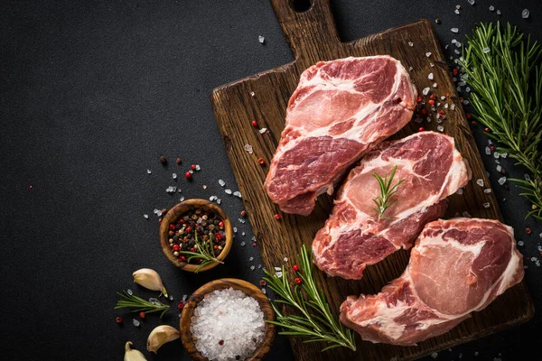 Carne de cerdo en tablero de madera sobre mesa negra. — Foto de Stock