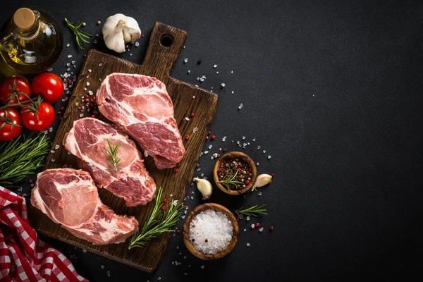 Carne de cerdo en tablero de madera sobre mesa negra. — Foto de Stock