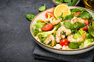 Taş masada yeşil yapraklı karides salatası..