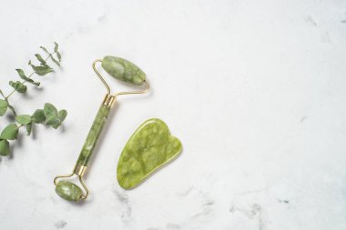 Yeşim silindir ve gua sha taş masajcısı mermer masada.