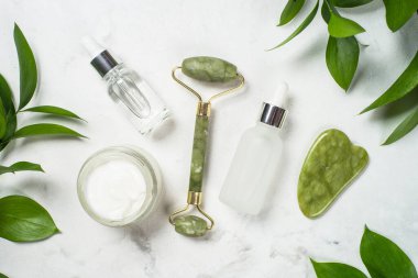 Yeşim silindir ve gua sha taş masaj aleti. Yüz kremi ve serum şişesiyle..