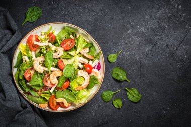 Taş masada yeşil yapraklı karides salatası..