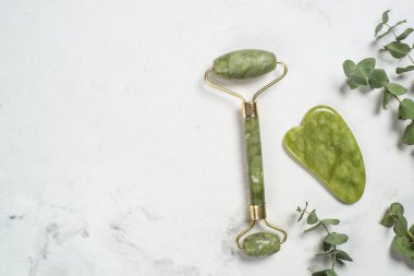 Yeşim silindir ve gua sha taş masajcısı mermer masada.