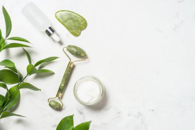 Yeşim silindir ve gua sha taş masaj aleti. Yüz kremi ve serum şişesiyle..