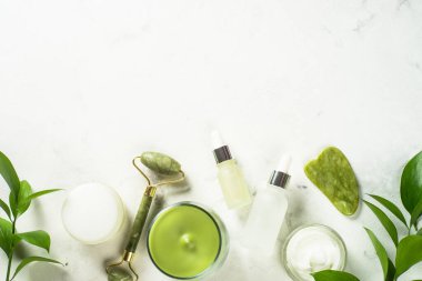 Yeşim silindir ve gua sha taş masaj aleti. Yüz kremi ve serum şişesiyle..