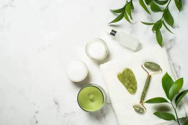 Jade rolo e água sha pedra massageador com creme facial e garrafa de soro. — Fotografia de Stock