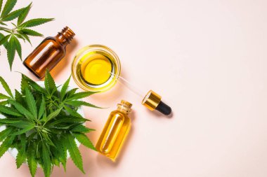 Cam şişelerde esrar yağı ve beyaz masada esrar yaprakları.