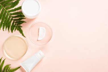 Kozmetik ürünleri ve yeşil bitkilerle dolu cam petri kabı.