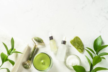 Yeşim silindir ve gua sha taş masaj aleti. Yüz kremi ve serum şişesiyle..