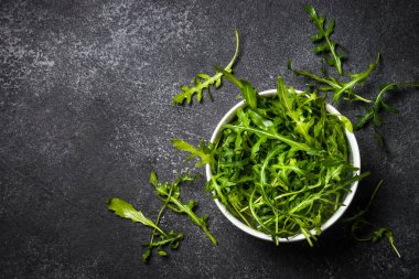 Arugula taze yeşil yapraklar siyah taş masada.