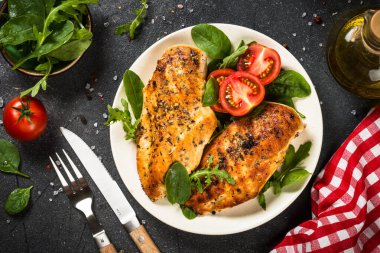 Siyah arka planda beyaz tabakta ızgara tavuk filetosu..