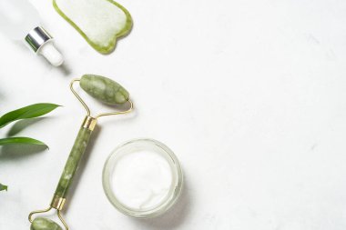 Yeşim silindir ve gua sha taş masaj aleti. Yüz kremi ve serum şişesiyle..