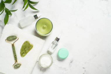 Yeşim silindir ve gua sha taş masaj aleti. Yüz kremi ve serum şişesiyle..