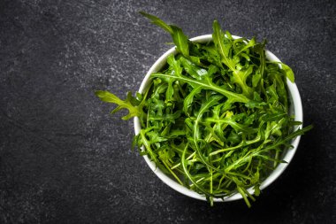 Arugula taze yeşil yapraklar siyah taş masada.