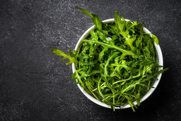 Arugula taze yeşil yapraklar siyah taş masada.