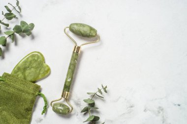 Yeşim silindir ve gua sha taş masajcısı mermer masada.