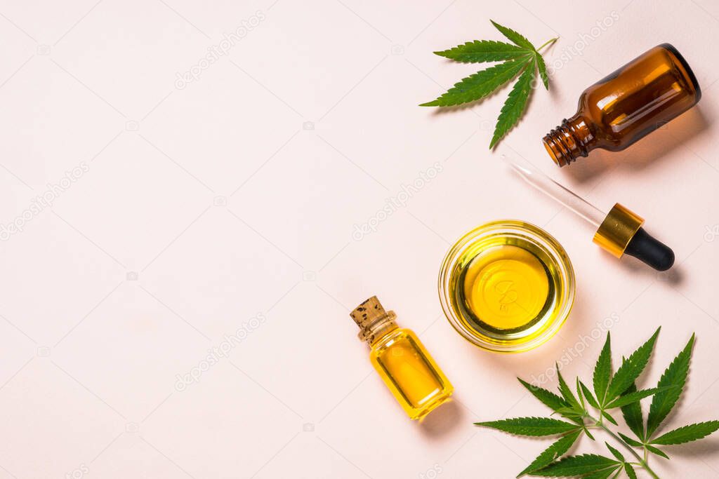Cannabis oil in glass bottles and cannabis leaves at white table.